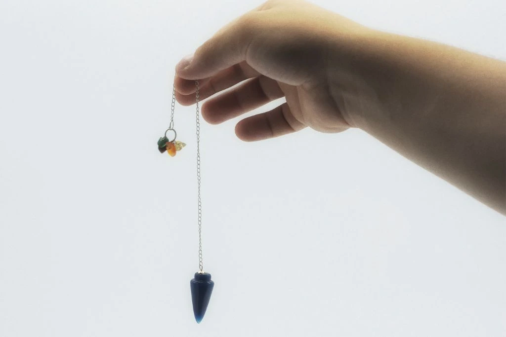 A person holding a Sodalite pendulum on a grayish background