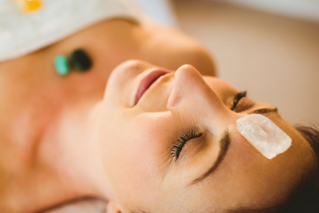 A woman laying down with a crystal placed on her forehead and chest.