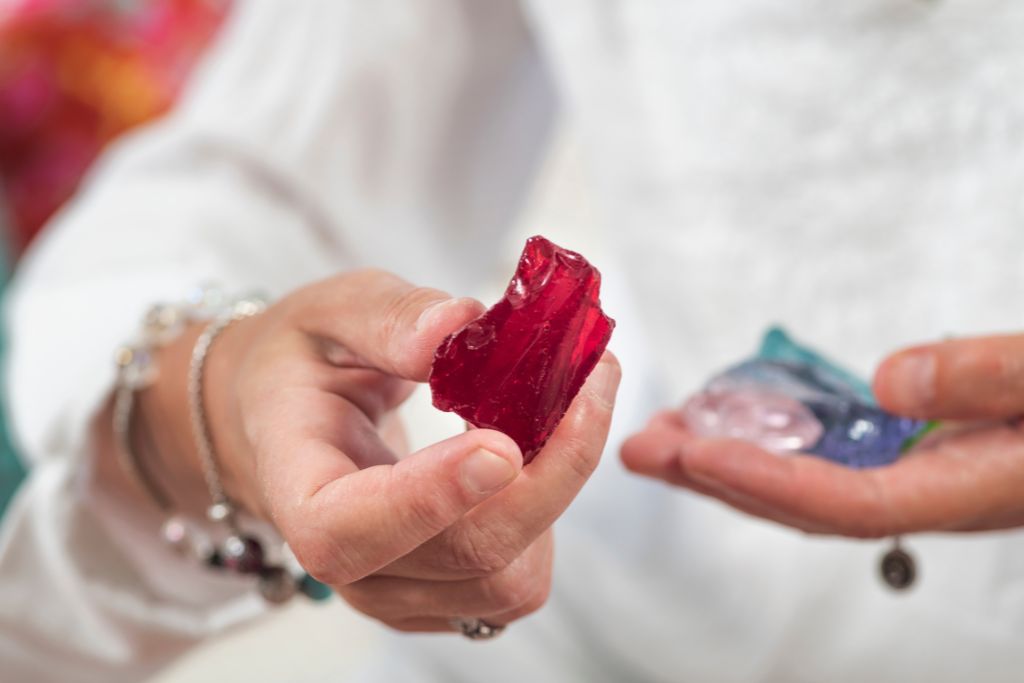 A woman extending her arm to offer a red crystal in her right while holding another crystal by her left hand.