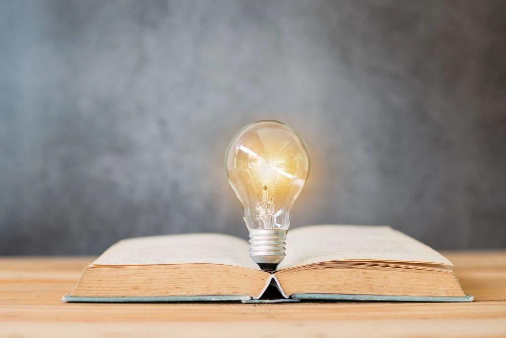 A lit bulb on top of an open book