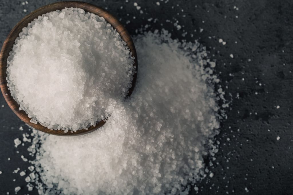 A wooden bowl that is full of salt on a black background