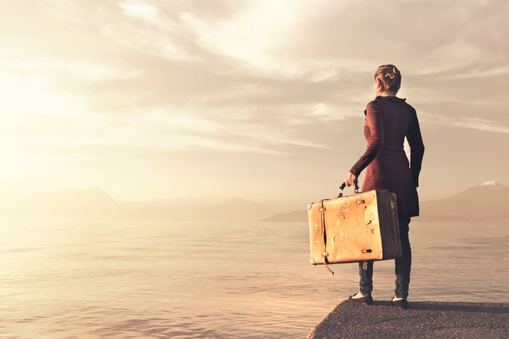 Woman by the ocean holding a suitcase looking at the faraway light. 