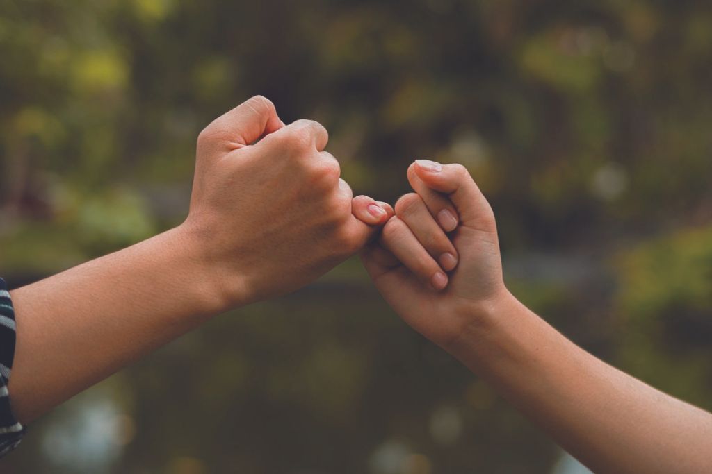 two hand doing pinky swear or pinky fingers entwined.
