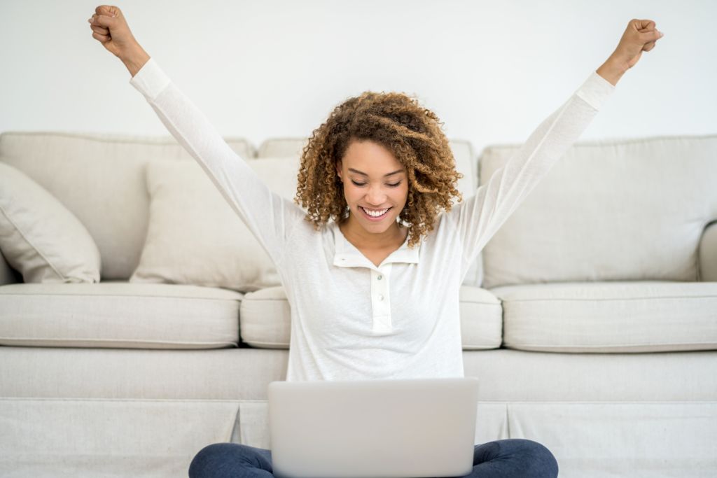 woman sitting on the floor with a laptop and hands in the air