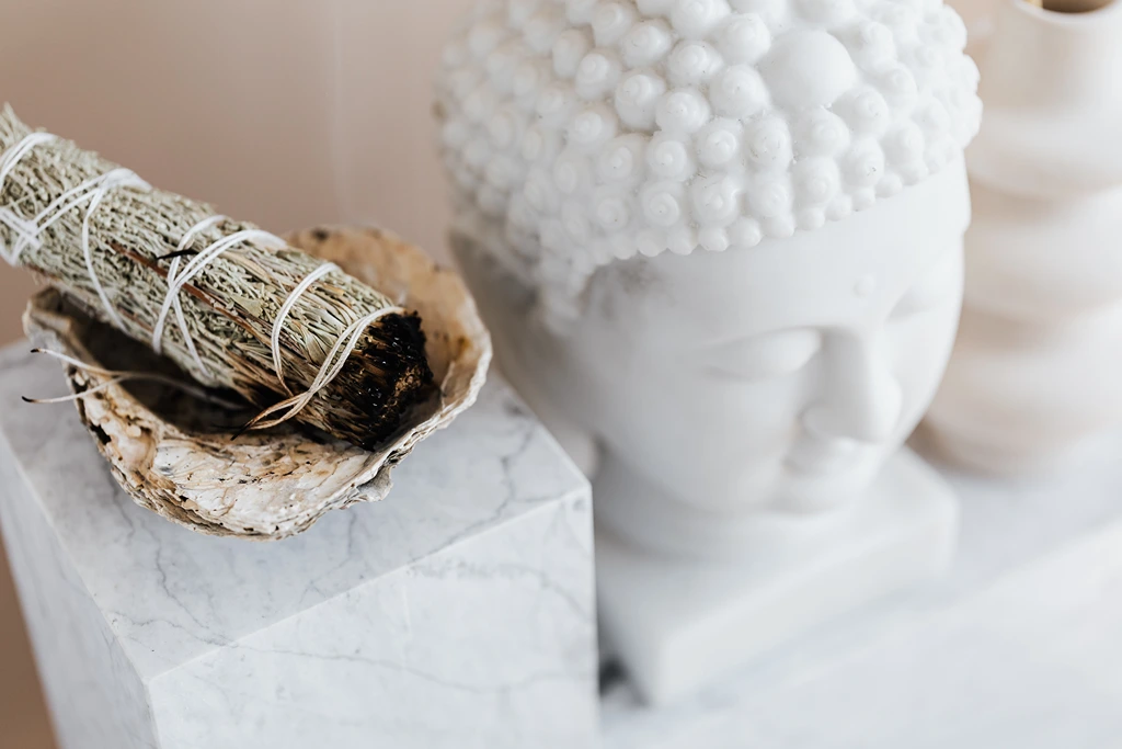 smudge stick on a ceramic cube beside a buddha figure