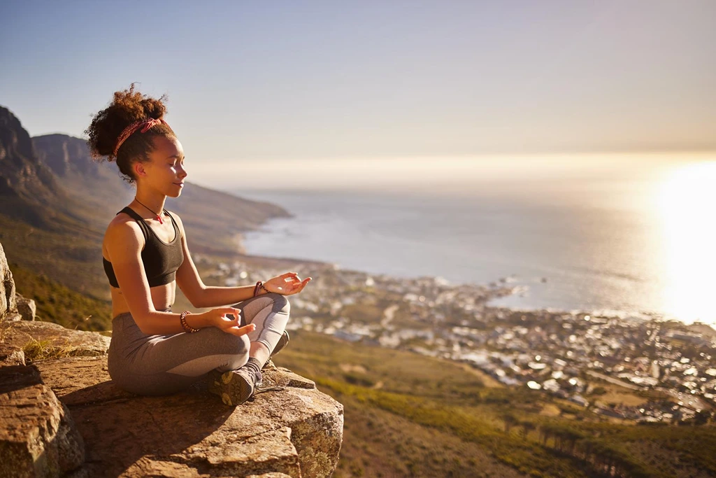 female model meditating on a cliff with ocean background