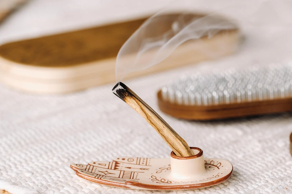 palo santo stick on an incense burner on top of a white woven table cloth