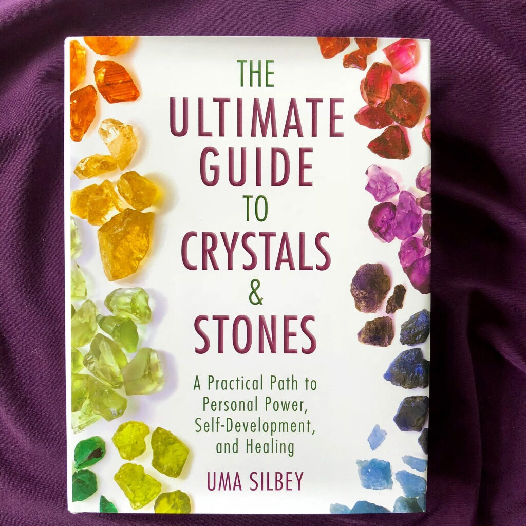 The Ultimate Guide to Crystals and Stones by Uma Silbey placed on top of a purple cloth