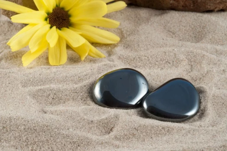 hematite stones placed on sand with a plastic sunflower on the back