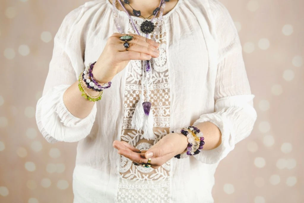 Woman wearing several crystal jewelries while holding an amethyst pendulum