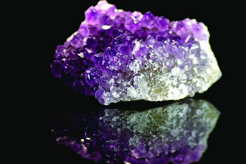 Shiny Amethyst crystal with a reflection on bottom left part on a black background