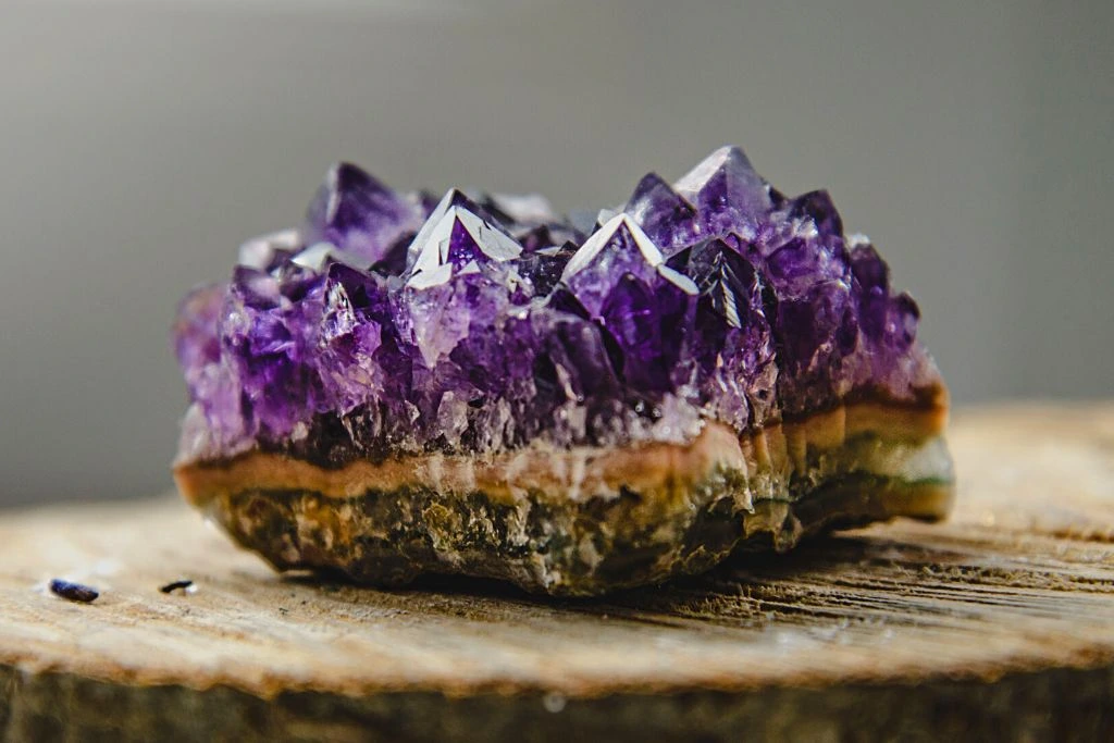Amethyst crystal placed on top of a natural wood with a gray blurred background 