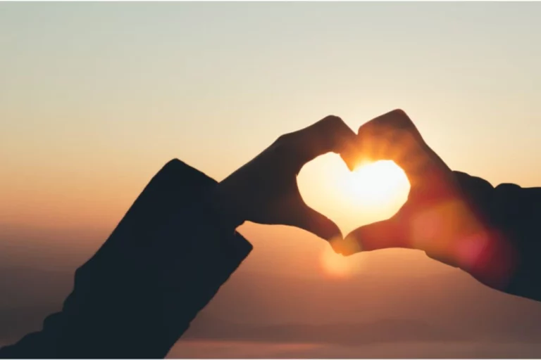 male and female hands forming a heart silhouette during sunset