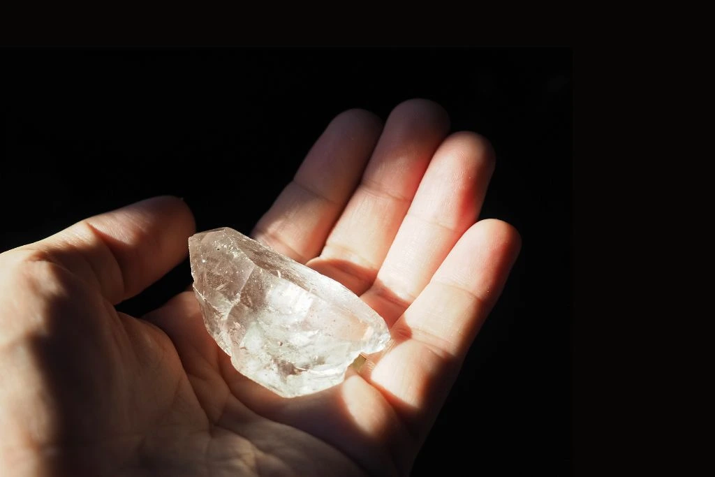 a person holding on his palm a clear quartz crystal
