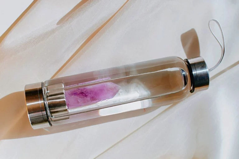 A water bottle with an amethyst crystal inside it, placed on a brown surface.
