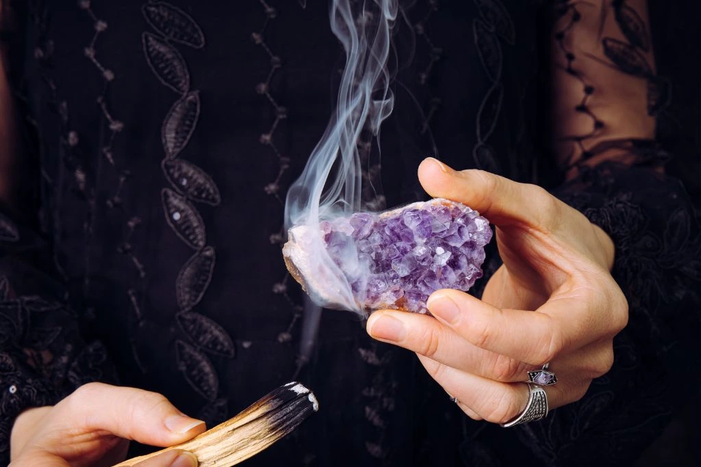 Woman holding an Amethyst crystal and cleansing it using fire and palo santo stick