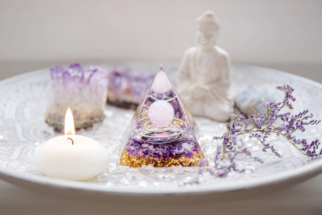 Orgone pyramid together with white candle and buddha figurine situated on a white ceramic plate