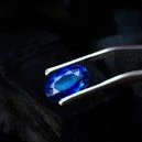 The tweezer is holding a Sapphire Gemstone on a black background