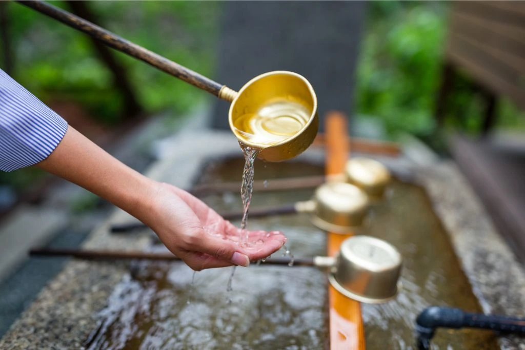 woman washing hands with clean water with a brass ladle