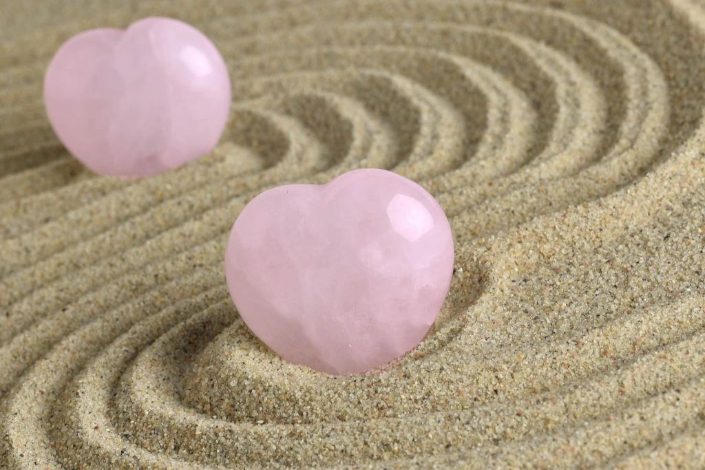 a rose quartz crystal shaped like a heart placed on a beach sand