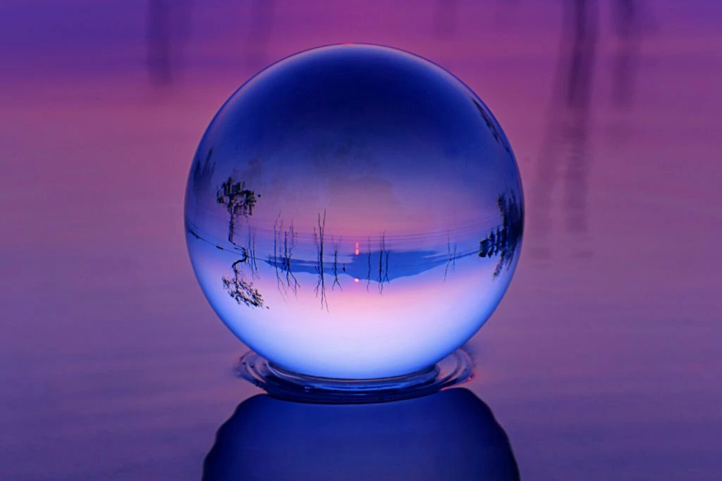 Crystal ball placed on a water with a pink sunset on the background