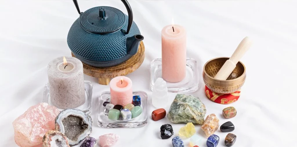 various crystals, a blue tea pot, candles and mortar and pestle on a white background