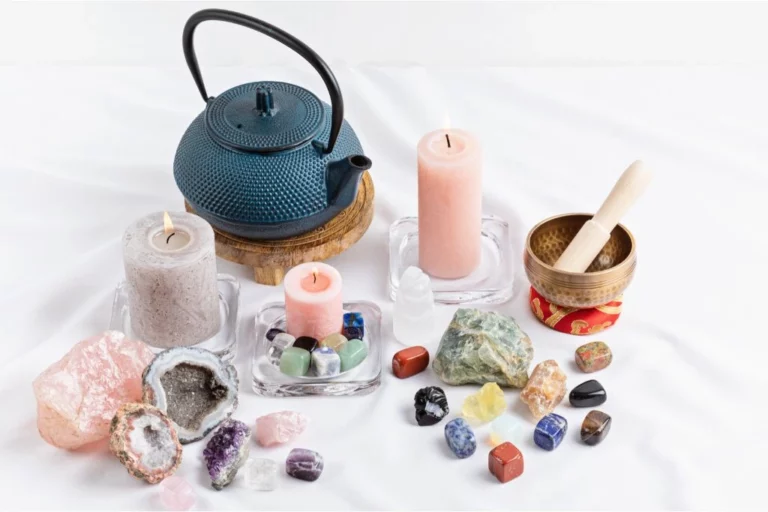 various crystals, a blue tea pot, candles and mortar and pestle on a white background