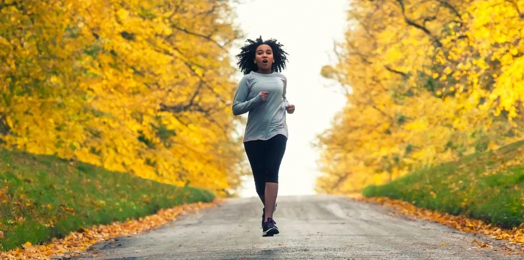 a woman jogging outside with trees around her
