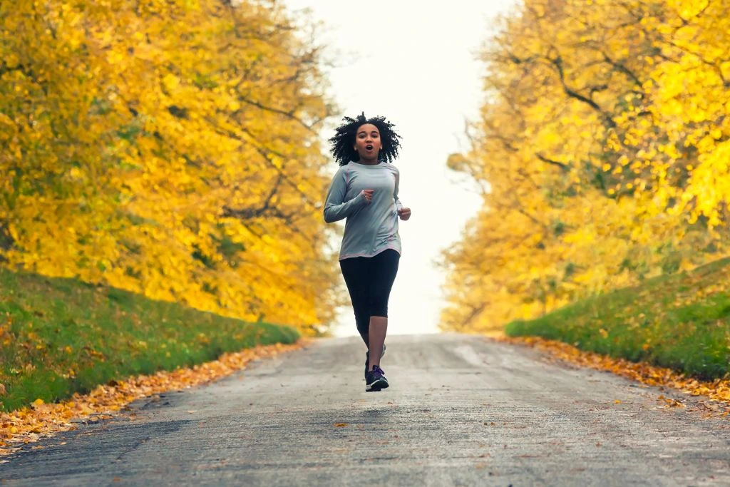 a woman jogging outside with trees around her