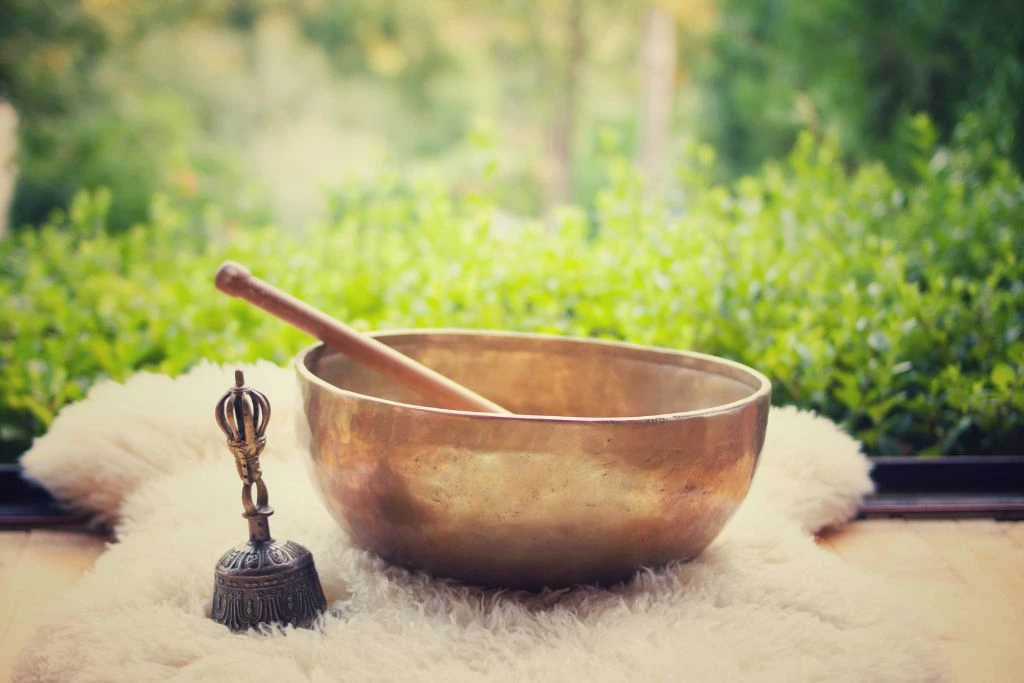 A copper singing bowl and a bell beside it on a fur cloth