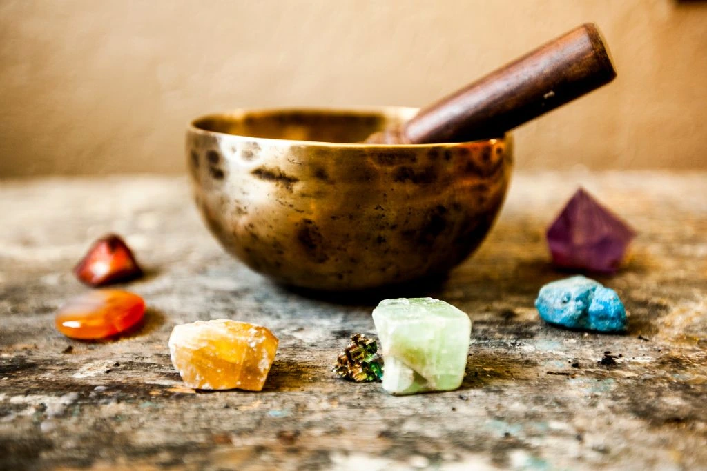 A singing bowl with different kinds of crystals beside it.