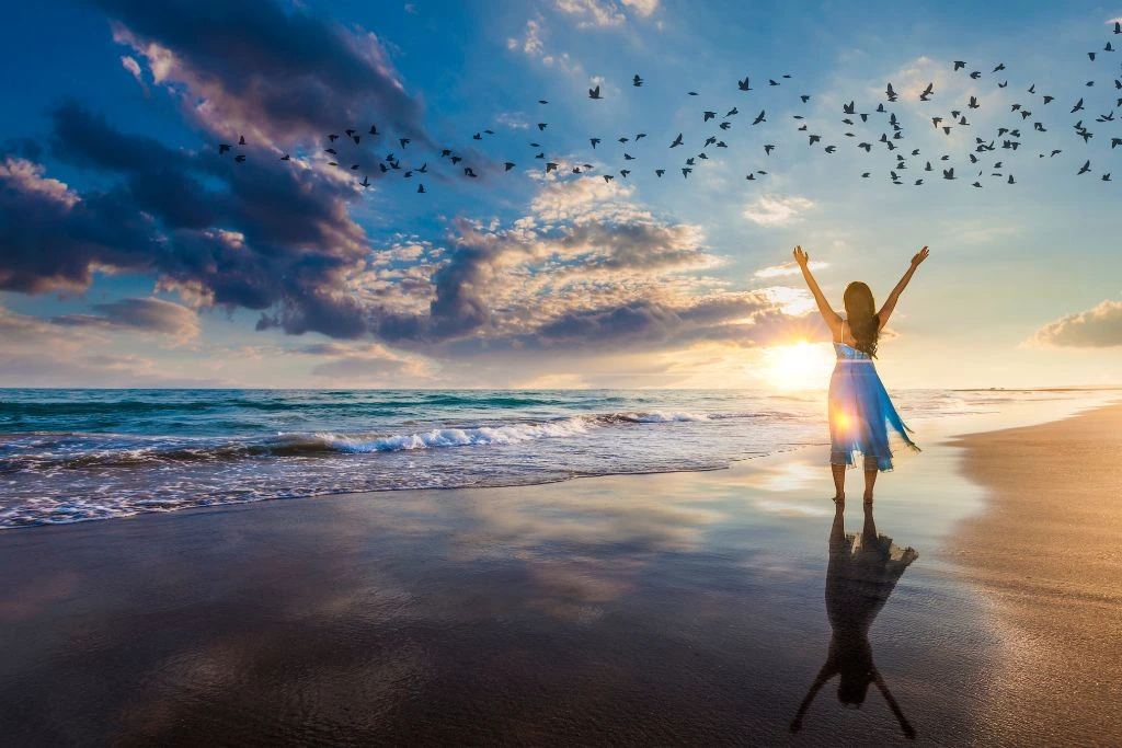 A woman raised two hands in the air near the beach