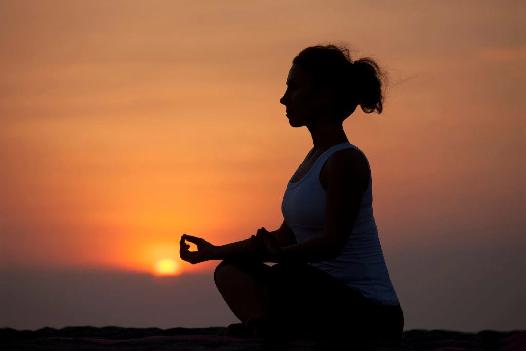 A woman meditating during the sunset