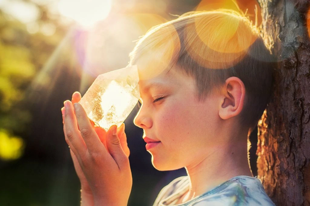 A young boy puts a crystal on his forehead in nature