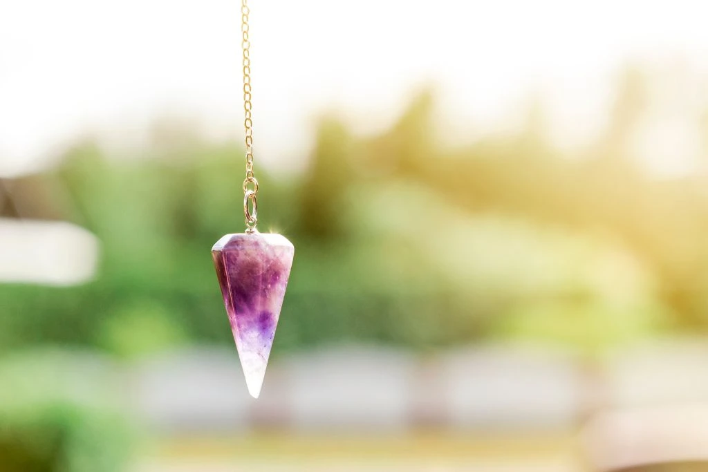 A hanging Amethyst Pendulum on a blurred backgroud