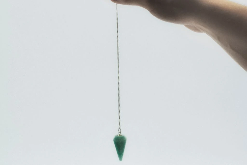 A person holding a Aventurine Pendulum on a beige background