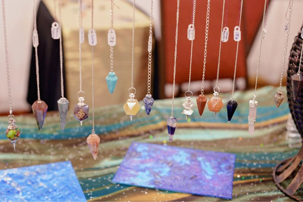 Different kinds of Crystal Pendulums hanging over a glittery table