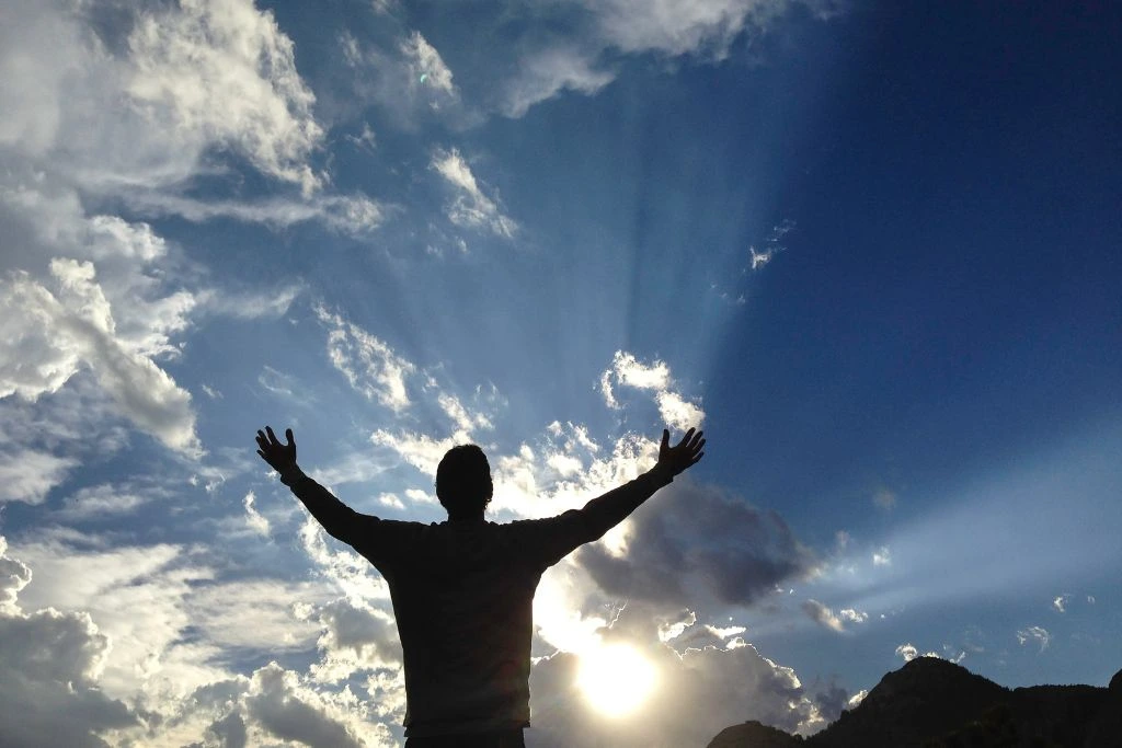 A person raised two hands in the air in front of the sun