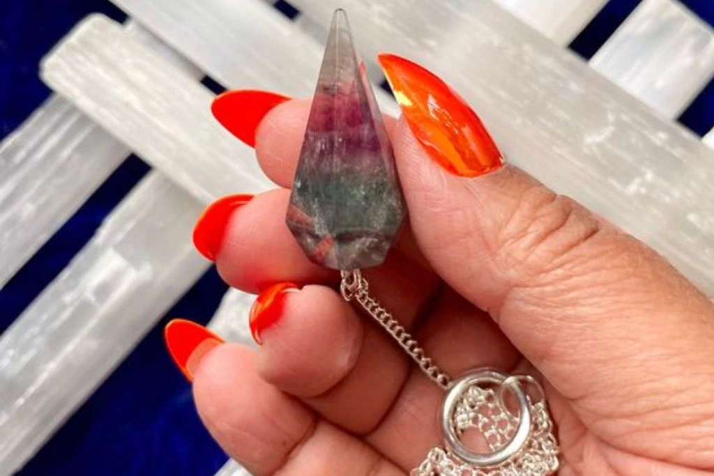 A person holding a Fluorite Pendulum with fluorite sticks on the background