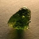 A Moldavite crystal on a brown background