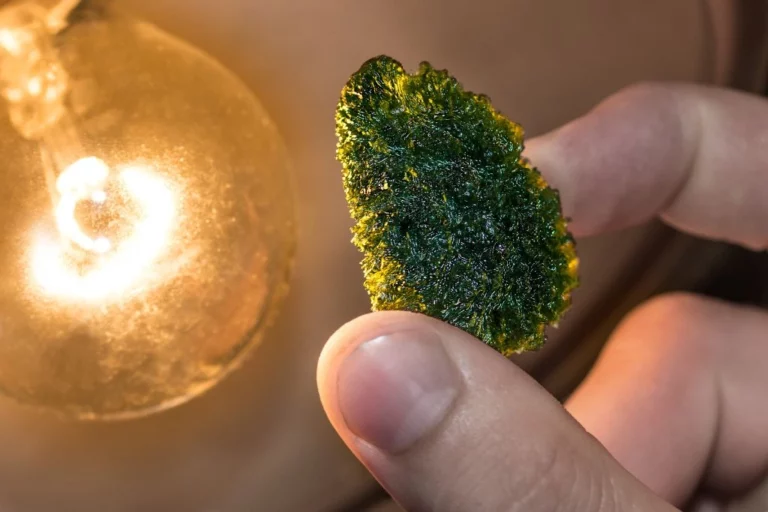 A person holding a moldavite crystal near the light bulb