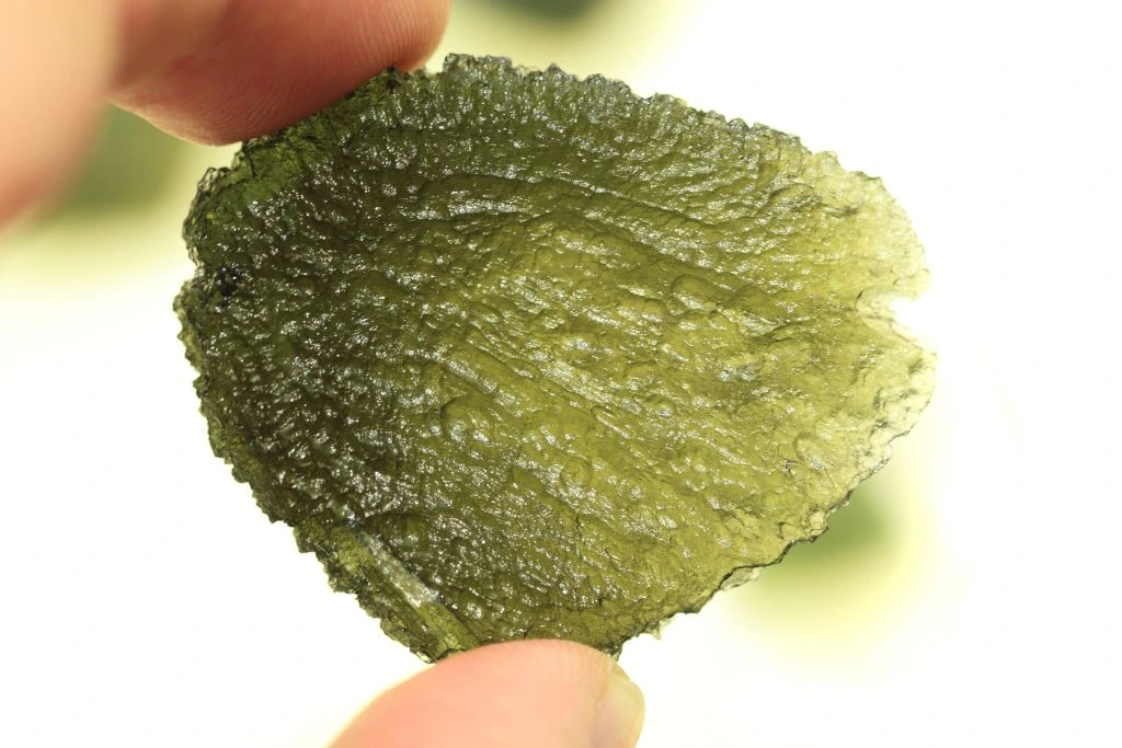 A person holding a raw Moldavite crystal