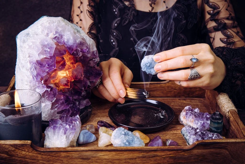 A woman smudging a celestite crystal in front of a tray of crystals