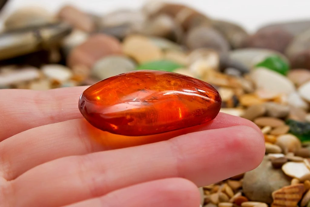Sunstone crystal placed on a hand with a blurry beach background