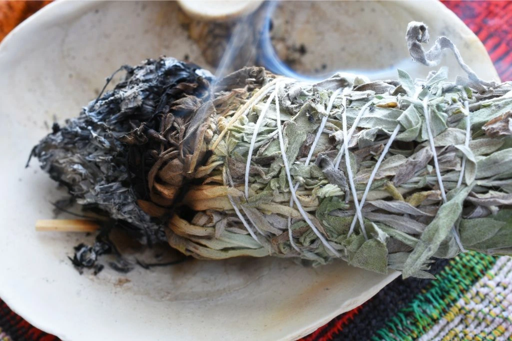 A burning white sage smudge stick in the bowl