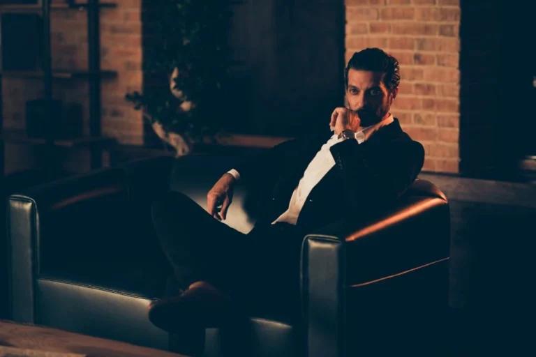 A man in formal wear with legs crossed sitting on a black sofa