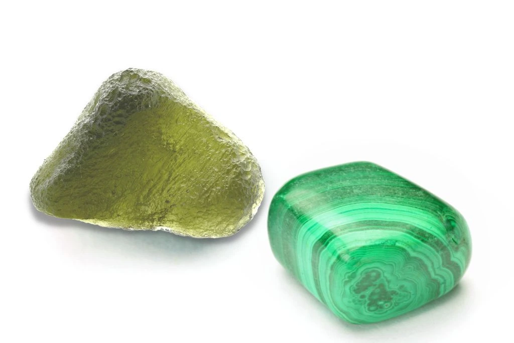 Moldavite crystal and malachite crystal are next to each other on a white background