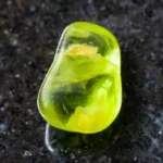 A peridot crystal on a black granite