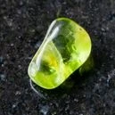 A polished peridot crystal on a black granite