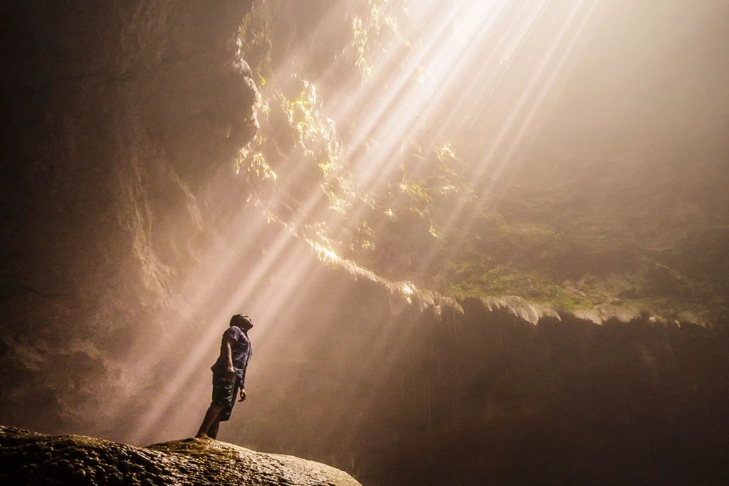 A man looking above the hole of the cave while standing on a rock